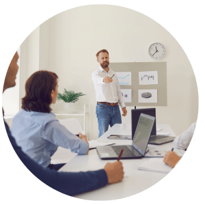 person speaking in a conference room to people seated around a table with laptops