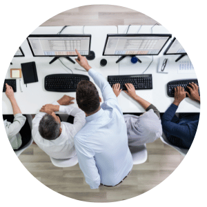 person pointing at a computer screen while four people work at a desk